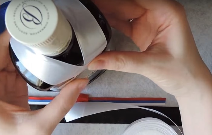 Gluing a white ribbon on a bottle of brandy