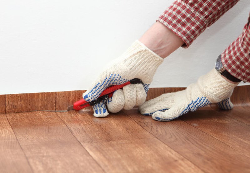 Do-it-yourself trimming of the edges of linoleum along the wall with a construction knife