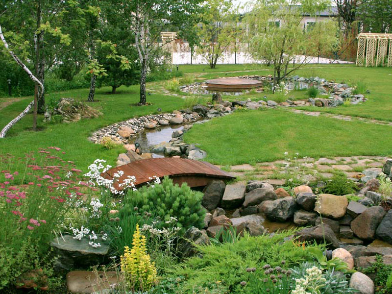 Garden lawn with stream and wooden bridge