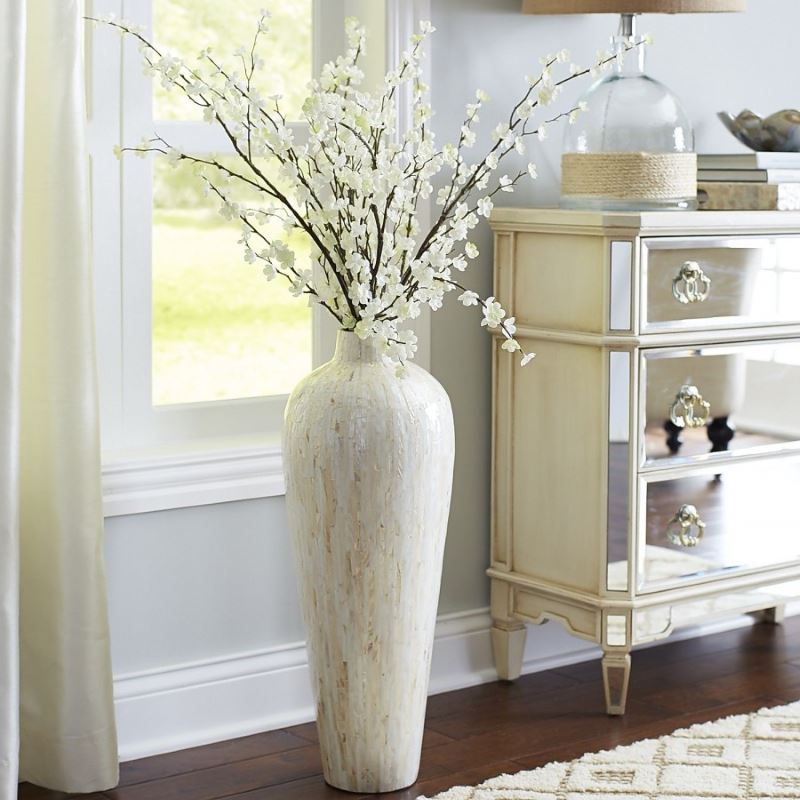 Light vase with flowering branches next to a vintage chest of drawers