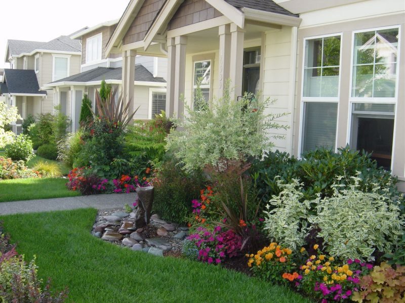 A flower bed with perennials in front of the porch of a country house